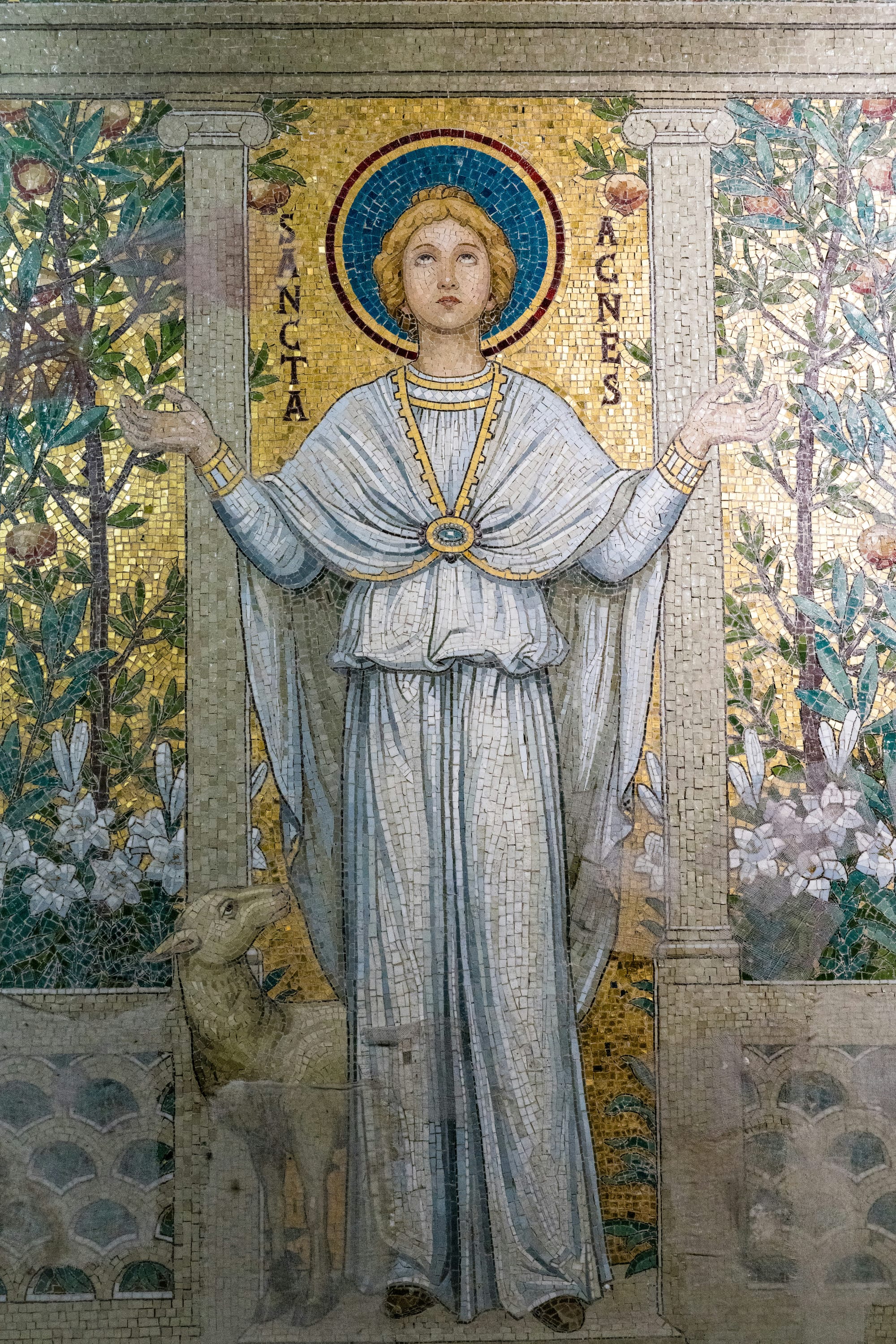 A mosaic of St Agnes, gazing toward heaven, in a white robe with a lamb at her feet.