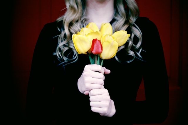 A woman in black holds a bouqet of tulips, all yellow save one red tulip in the middle.