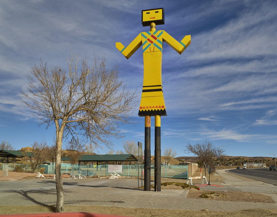 A huge sculpture of a Native American doll in a pose of welcome stands at the entrance to a park.
