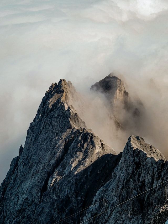 The sun shines on one side of a range of mountain peaks shrouded in cloud.