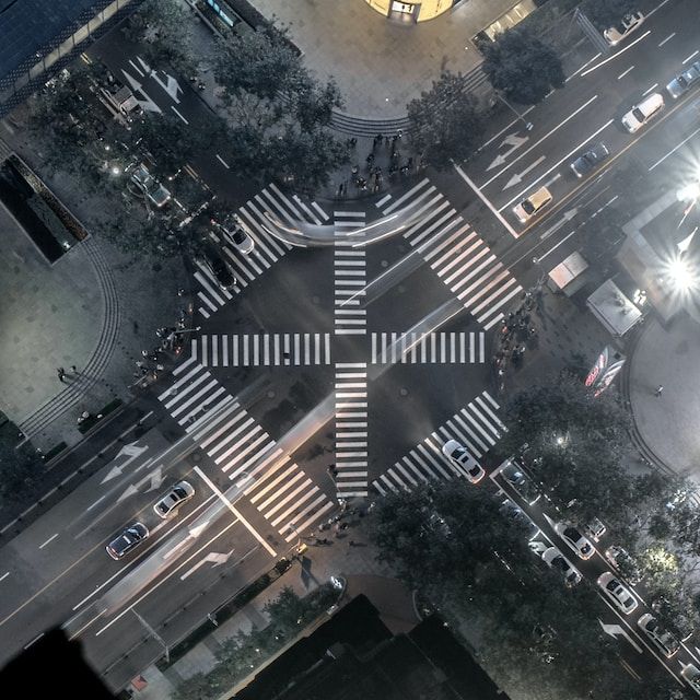 An aerial view of a busy street crossing with many cars and pedestrian crosswalks connecting all four corners.