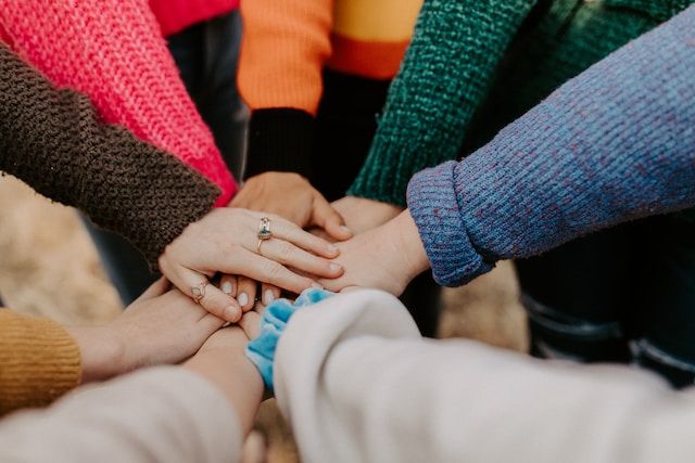 Seven people reaching in to join hands in a circle.